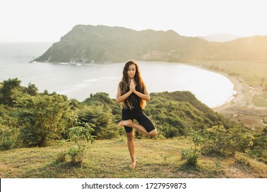 Young woman practicing yoga poses at sunset with beautiful ocean and mountain view. Sensitivity to nature. Active lifestyle. Spiritual and emotional concept.