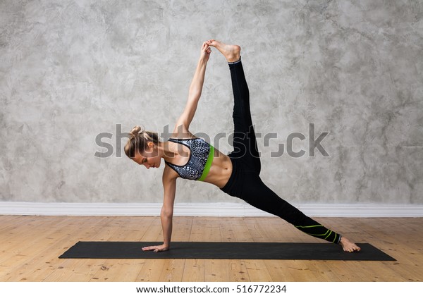 Young woman\
practicing yoga Side plank pose, Vasisthasana advanced against\
texturized wall / urban background\
