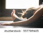 Young woman practicing yoga, sitting in Seated forward bend exercise, paschimottanasana pose, working out, wearing sportswear, grey pants, bra, indoor, home interior background, close up