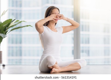 Young Woman Practicing Yoga, Sitting In Sukhasana Pose, Performing Humming Bee Breathing Exercise, Bhramari Pranayama Technique, Working Out, Wearing Sportswear, White T-shirt, Pants, Full Length 