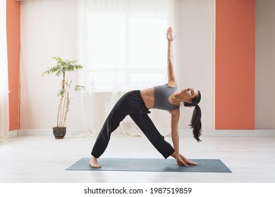 Young woman practicing yoga, standing on the mat, performs the exercise utthita trikonasana, triangle pose.