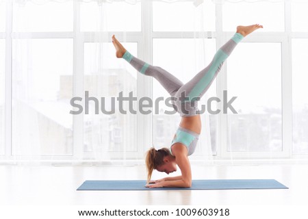 Young woman practicing yoga, standing in Pincha Mayurasana - Forearm stand at the yoga studio