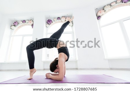 Young woman practicing yoga, standing in handstand exercise, working out, wearing black sportswear, on the floor near window