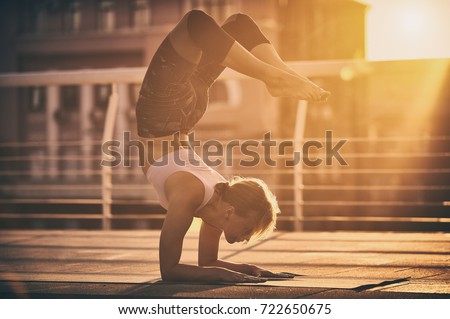 Young woman practicing yoga, standing in Vrischikasana Scorpion pose in the terrace at sunset