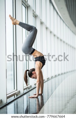 Young woman practicing yoga standing in handstand exercise, Pincha Mayurasana pose working out, against panoramic window