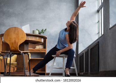 Young woman practicing yoga, stretching in Extended Side Angle exercise, Utthita parsvakonasana pose, working out at home sitting on chair.
