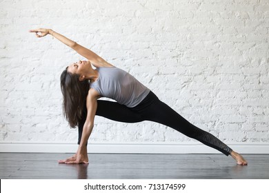 Young Woman Practicing Yoga, Stretching In Utthita Parsvakonasana Exercise, Extended Side Angle Pose, Working Out, Wearing Sportswear, Gray Tank Top, Black Pants, Indoor Full Length, Studio Background