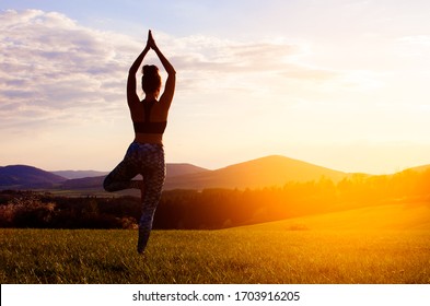 Young Woman Practicing Yoga With Sunset In Nature