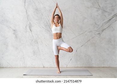 Young woman practicing yoga Tree pose, Vrikshasana against texturized wall background