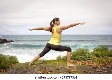 Young Woman Practicing Yoga Warrior Pose Near The Ocean