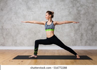 Young woman practicing yoga Warrior pose, Virabhadrasana against texturized wall / urban background 