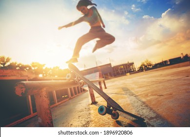 Young Woman Practising Skateboarding At Skate Park. Women Try To Playing Skateboard Jumping At The Roll Bar With Sunset Background.