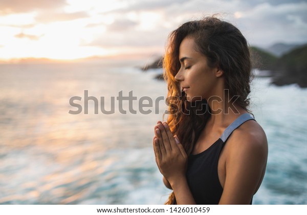 Young\
woman praying and meditating alone at sunset with beautiful ocean\
and mountain view. Self-analysis and soul-searching. Spiritual and\
emotional concept. Introspection and soul\
healing.