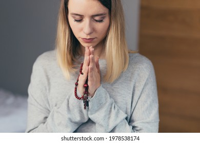 Young woman prays to God, folded her arms on her chest uses a rosary and a crucifix, asks for a better fate