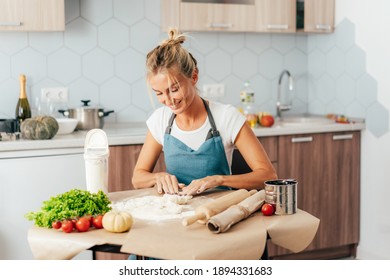 Young woman prepares dinner from ingredients of vegetables and dough at the table in the kitchen.