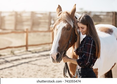 Young woman preparing to become a riding instructor taking care and talking to a horse on a hot autumn day.