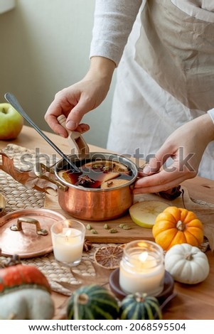 Young woman preparing hot autumn drink: mulled wine with spices, fruits. Natural ingreduents: cinnamon, anise, cardamon, clove, apple, orange. Cozy home atmosphere
