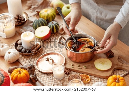 Young woman preparing hot autumn drink: mulled wine with spices, fruits. Natural ingreduents: cinnamon, anise, cardamon, clove, apple, orange. Cozy home atmosphere