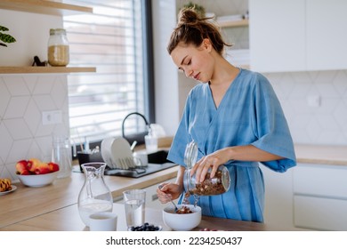 Young woman preparing muesli for breakfast in her kitchen, morning routine and healthy lifestyle concept. - Powered by Shutterstock