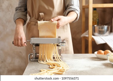 Young woman preparing noodles with pasta maker at table - Powered by Shutterstock