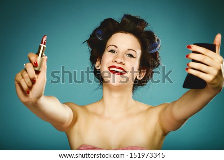 young woman preparing to party having fun, girl styling hair with curlers applying make red lipstick in hand up retro style blue background