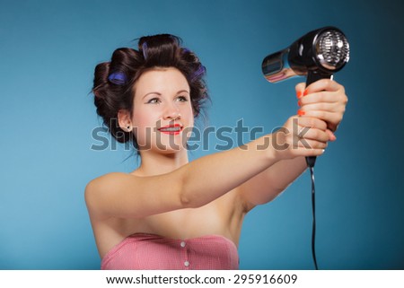 Young woman preparing to party having fun, funny girl styling hair with hairdreyer retro style on blue