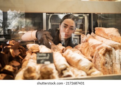 Young woman preparing pastry for sale in supermarket bakery department. Bakery female seller.