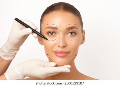 Young woman preparing for plastic surgery session, doctor in medical gloves contouring female patient face, isolated on white background - Powered by Shutterstock