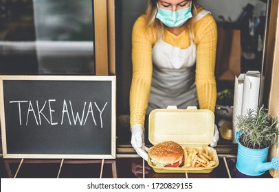 Young Woman Preparing Takeaway Food Inside Restaurant During Coronavirus Outbreak Time - Worker Inside Kitchen Cooking Fast Food For Online Order Service - Focus On Hamburger