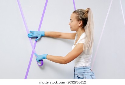 Young Woman Preparing Wall For Painting Standing On Ladder Applying Masking Tape On Wall. Diy Project