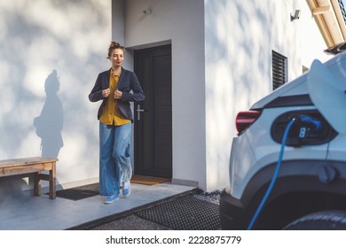 Young woman preparing to work while her electric car charging in home, sustainable and economic transportation concept.
