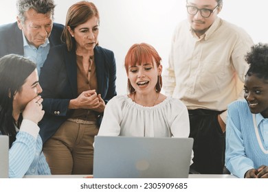 Young woman presenting project to diverse colleagues in office. She sits at her office desk, laptop open, while her multigenerational and multiracial team observes with interest and smiles. - Powered by Shutterstock