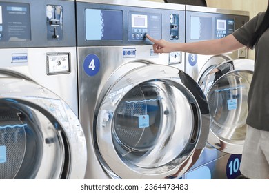 Young woman press the button to start the washing machine. Industrial laundry machines in laundromat in a public laundromat. Self-service laundry facility with many automatic washing machines. wash. - Powered by Shutterstock