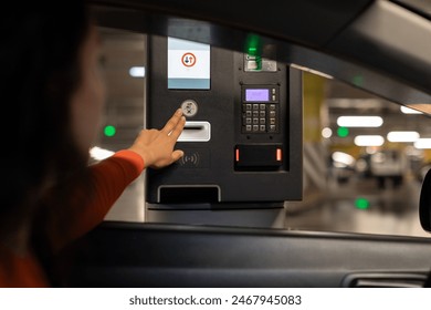 Young woman pressing button and waiting for the ticket at the parking meter at underground parking garage in shopping mall
