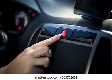 Young woman pressing emergency button on car dashboard 
