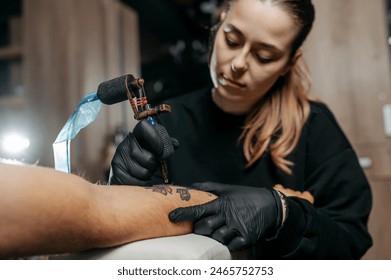 Young woman professional tattoo artist in black gloves making a rose tattoo on a man's forearm. She is holding  a tattoo machine. - Powered by Shutterstock