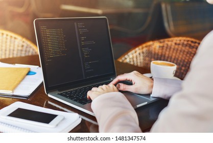 Young woman programmer writing code on laptop in cafe and drinking morning coffee, background