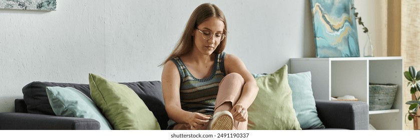 A young woman with a prosthetic leg sits on a couch in her modern living room, tying her shoes. - Powered by Shutterstock