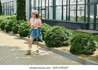 A young woman with a prosthetic leg walks through a city park, using her phone and enjoying a summer day. - Powered by Shutterstock