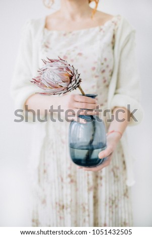 Young woman with protea flower in blue vase.