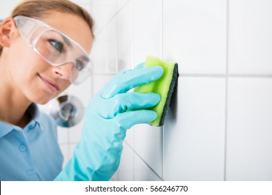 Young Woman With Protective Eyewear Cleaning The White Tile Of The Wall Using Sponge