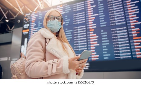 Young Woman In Protective Mask With Backpack In Front Of Information Board In Airport Terminal. Concept Online Checkin For Plane.