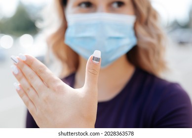 Young Woman In Protective Medical Face Mask Shows Manicure Barcode On Nail. Modern Technologies. Selective Focus On The Finger