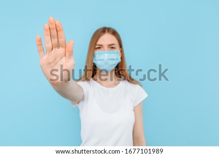 A young woman in a protective sterile medical mask on her face from infections, shows her hand, arm, and foot. Air pollution, virus, Chinese pandemic coronavirus concept, on an blue background