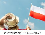 A young woman proudly holds the Polish flag above her head, against the sky with her other hand holding her hat, Concept of national holidays and patriotic events