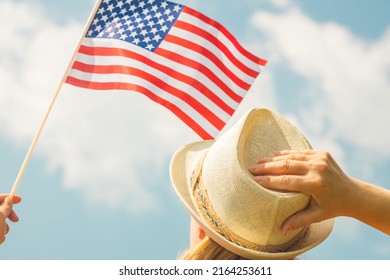 Young woman proudly holds the USA flag above her head while holding up her hat with her other hand, Concept of national holidays and patriotic events