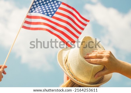 Young woman proudly holds the USA flag above her head while holding up her hat with her other hand, Concept of national holidays and patriotic events