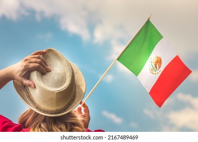 A young woman proudly raises the flag of Mexico above her head against the sky, The other hand holds up her hat, Concept for national holidays and patriotic events