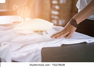 Young Woman Pull Out Paper From Waterproof Film On Fabric. Worker Working On Manual Screen Printing On T-shirt At Her Shop.