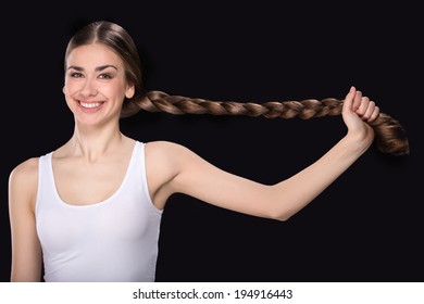 Young Woman Pulling Long Plait. Beautiful Girl Waist Up Holding Hair On Black Background